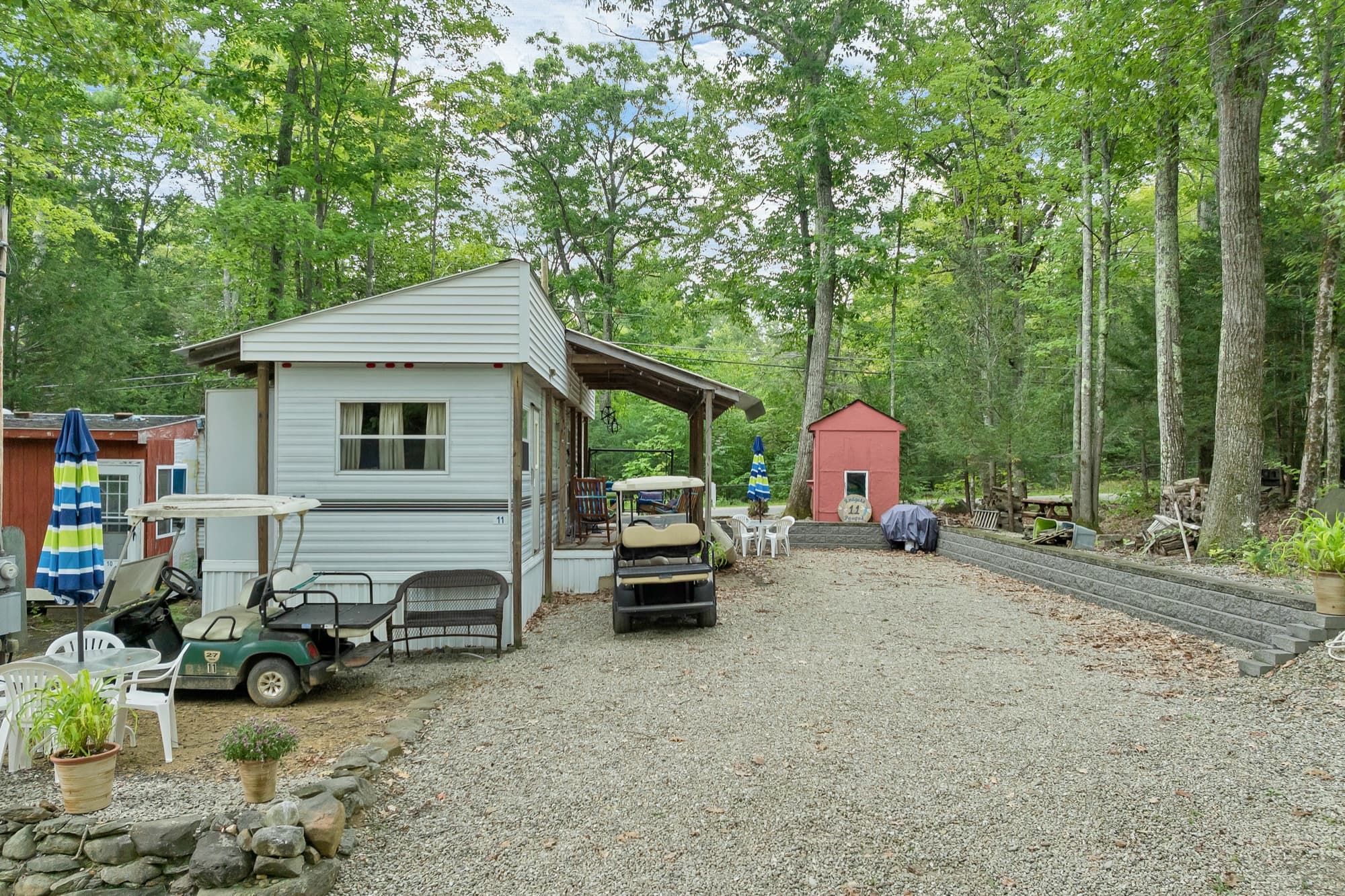 The gravel site from the drive, with the unit, the red shed, and the woods behind