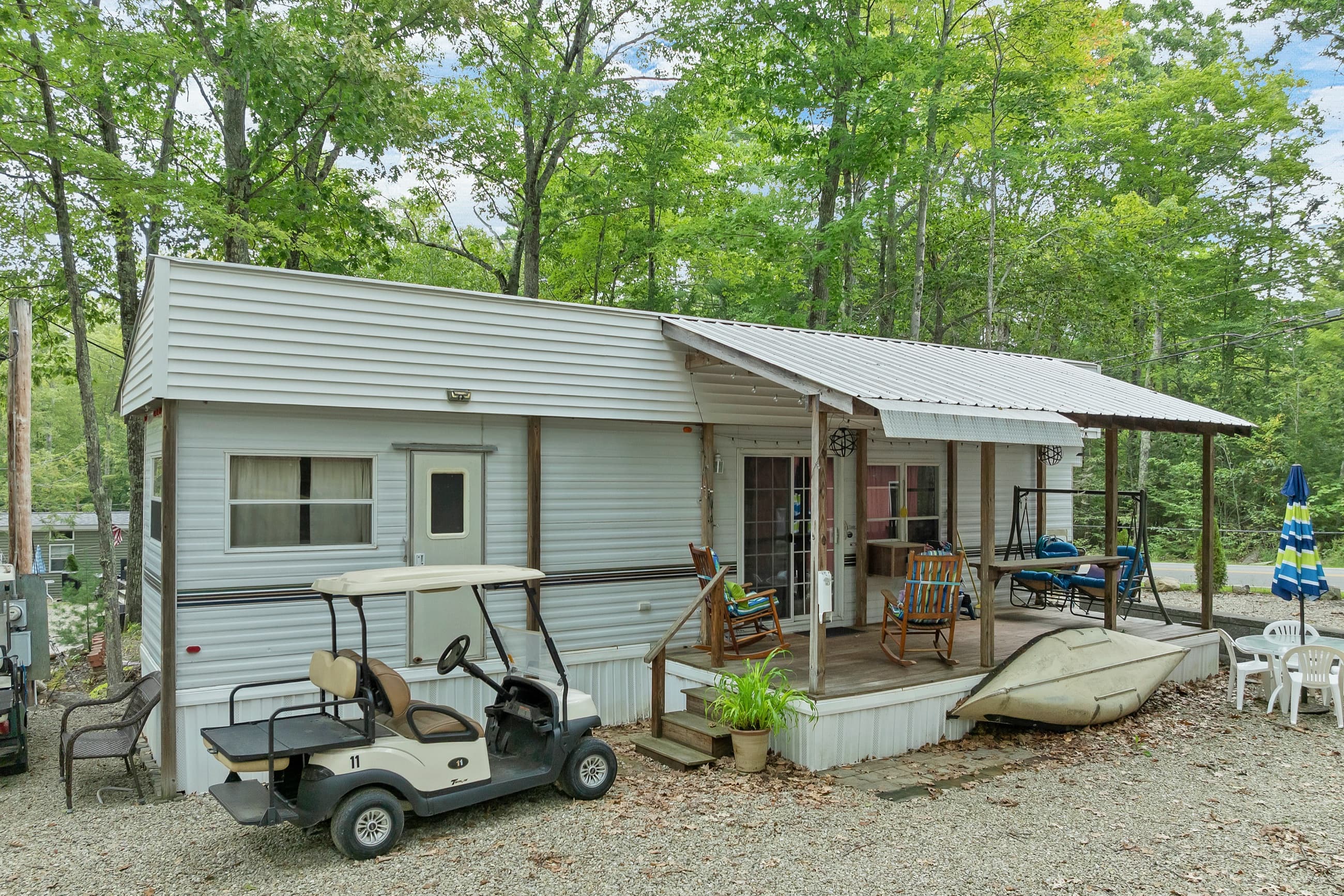 The white park model from the site, with the covered deck, a golf cart, and a kayak